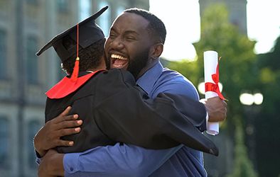 Gradating student, wearing their cap and gown, and hugging their family member